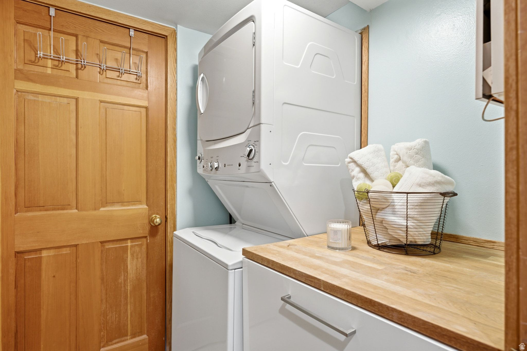 Laundry area featuring a stacked washer and dryer, wood-finish countertop, and a light blue wall finish