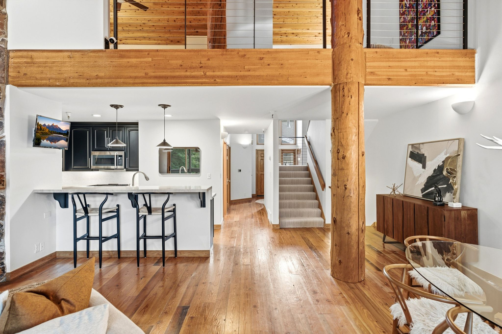 Open-concept interior featuring wood-finish flooring, a kitchen bar with pendant lighting, black cabinetry, and a prominent timber support column