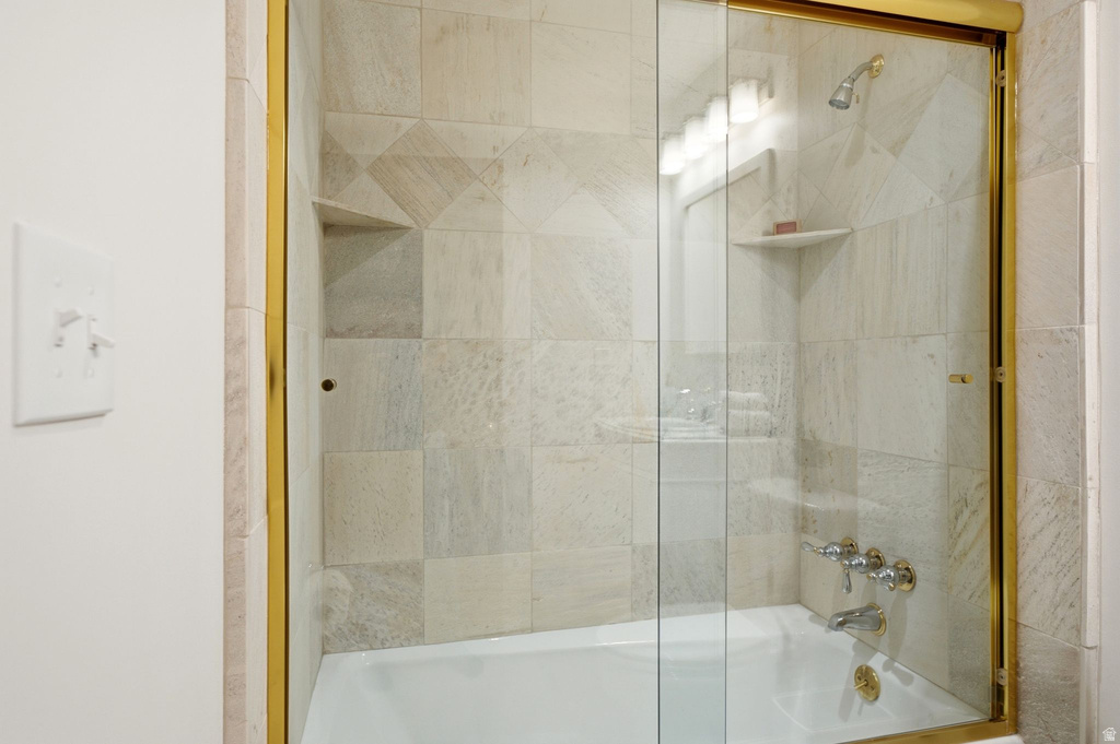Tub and shower combination featuring a glass enclosure with gold-tone framing, tiled walls, built-in shower niches, and a showerhead with accompanying fixtures