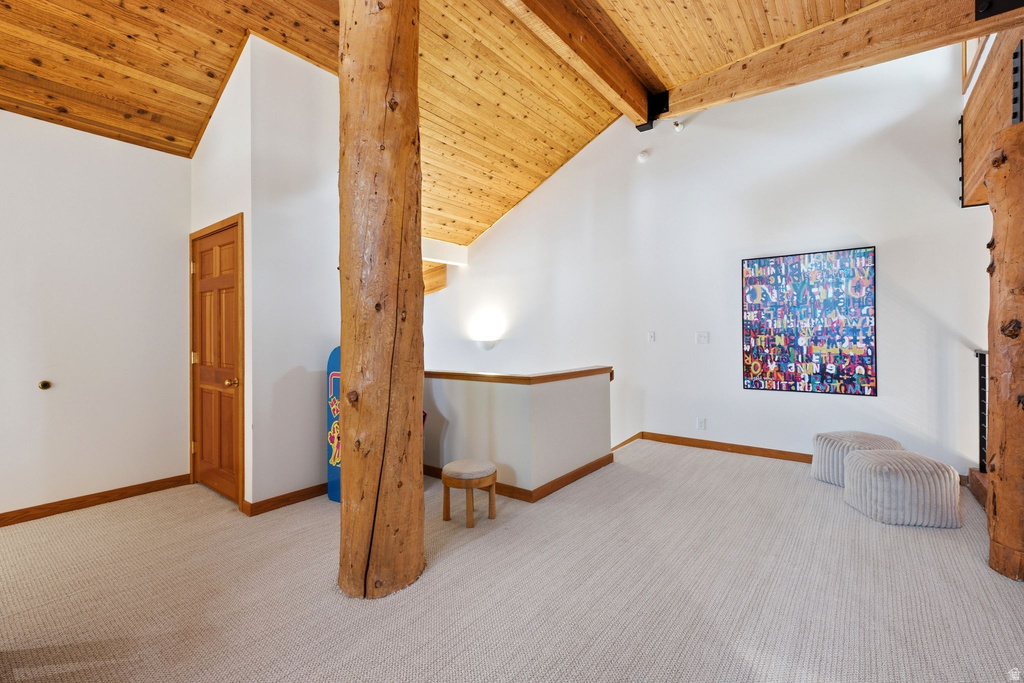 Vaulted wood-plank ceilings featuring exposed wood beams, bright white walls, light-toned carpeting, and a natural wood door