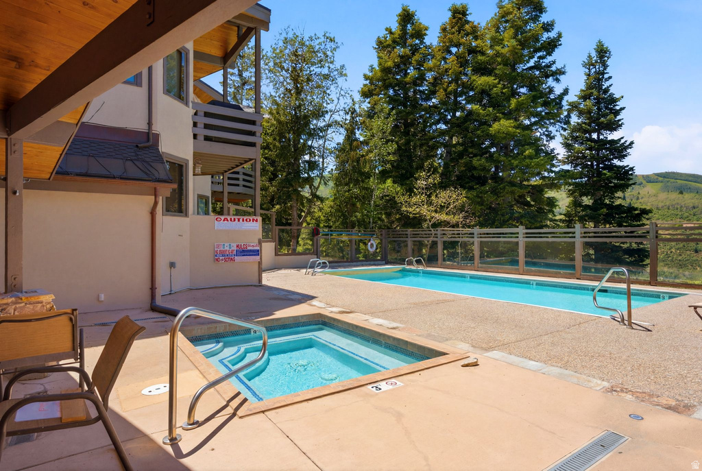 Outdoor concrete patio featuring a hot tub and an in-ground swimming pool