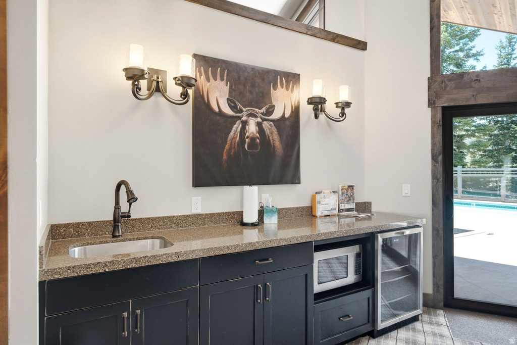 Wet bar featuring a stainless steel sink, dark cabinetry, built-in microwave, and beverage cooler