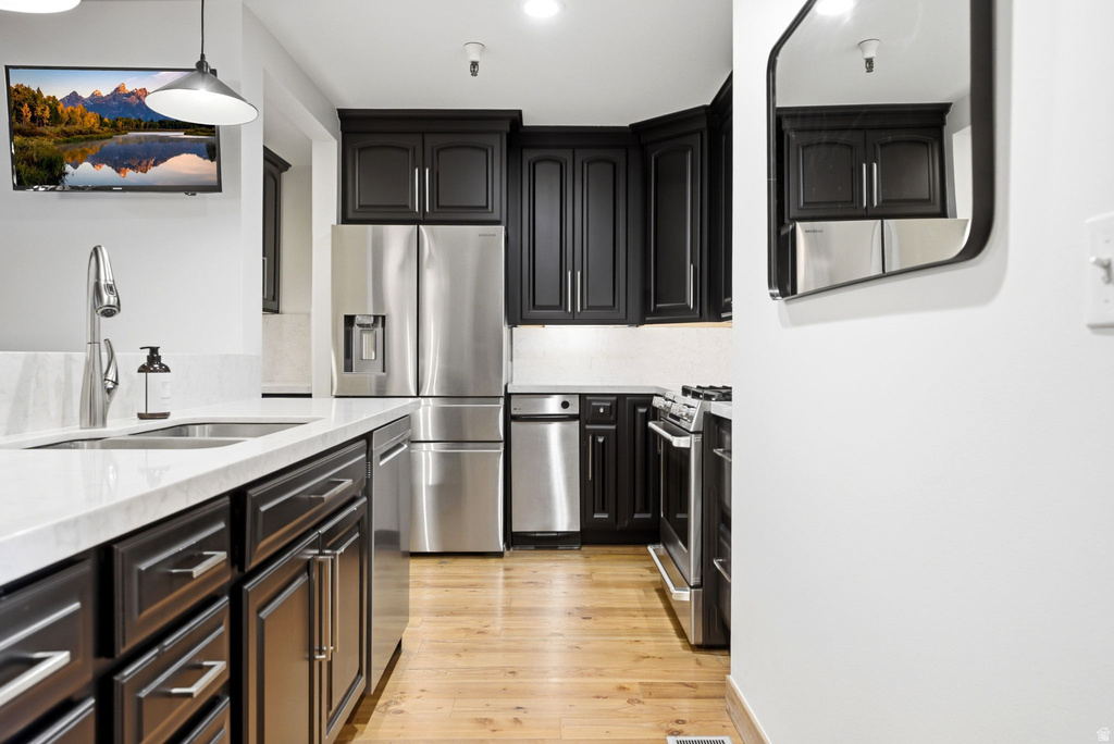 Kitchen featuring dark cabinetry, stainless steel appliances, light countertops, and wood-finish flooring