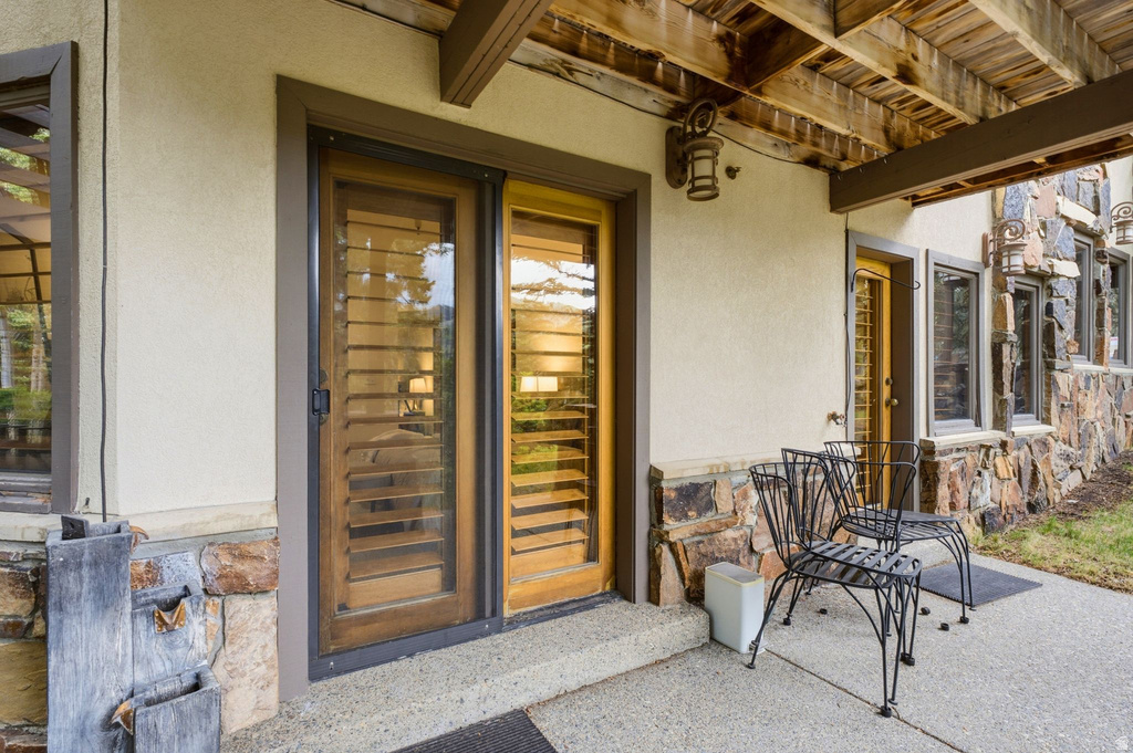 Stucco exterior with stone veneer accents, featuring a covered patio with exposed wood joists and a sliding glass door with interior plantation shutters