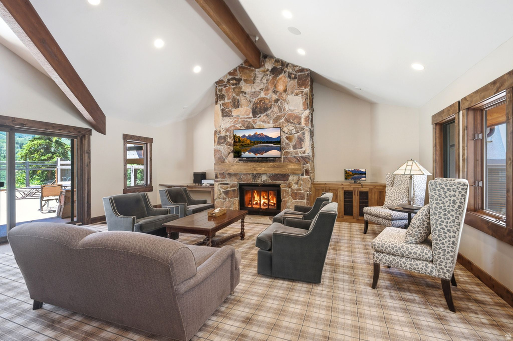 Spacious living area featuring a vaulted ceiling with exposed wood beams, a stone-clad fireplace, and a large sliding glass door opening to an outdoor deck