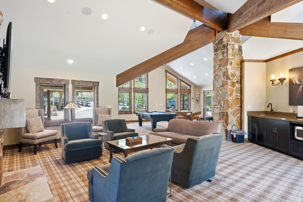 Spacious common area featuring a stone column, exposed wood beams, and vaulted ceilings