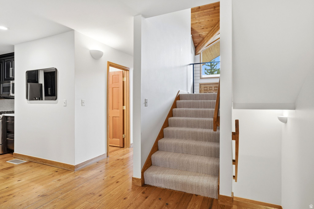 Carpeted staircase with wooden railing and vaulted wood-paneled ceiling