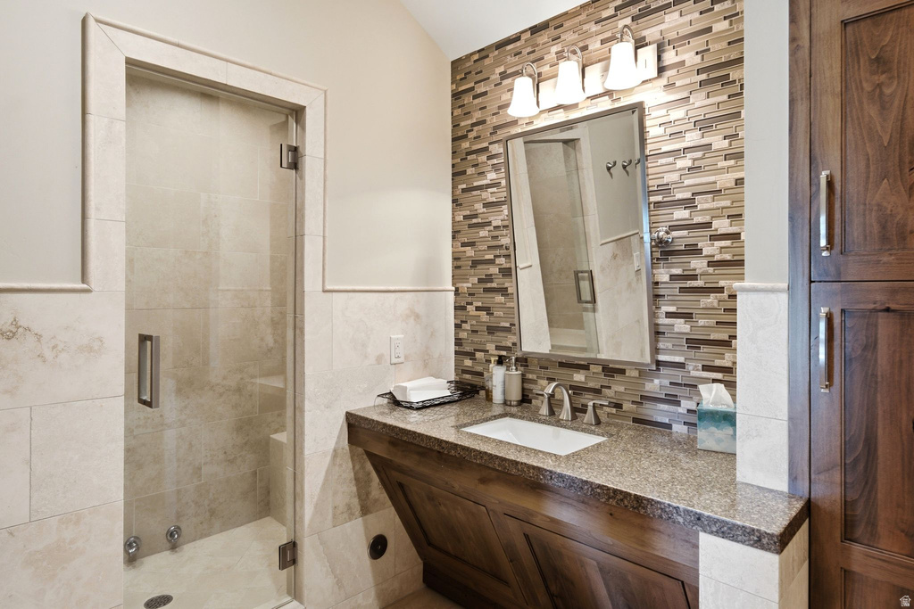 Bathroom featuring a glass-enclosed shower, a built-in shower bench, a vanity with a granite-style countertop, a rectangular undermount sink, and a multi-tone mosaic tile backsplash