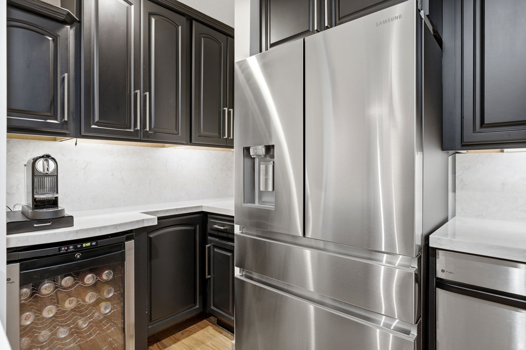 Modern kitchen featuring stainless steel appliances, dark wood cabinetry, light countertops, a built-in wine refrigerator, and under-cabinet lighting