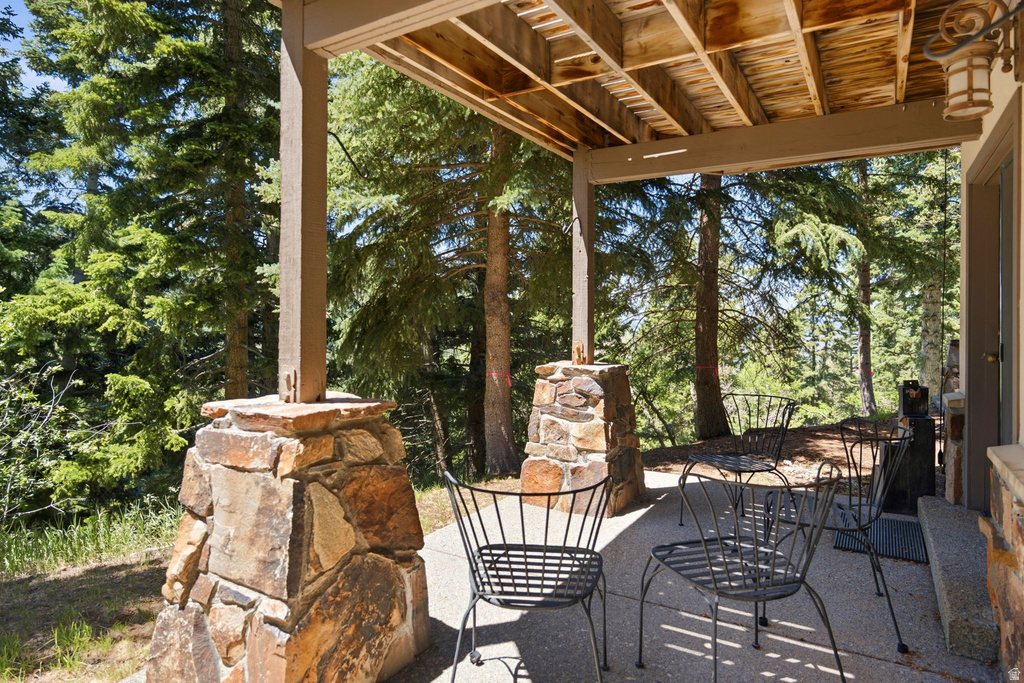 Covered outdoor patio area featuring robust stone-clad pillars, a concrete surface, and wood soffit