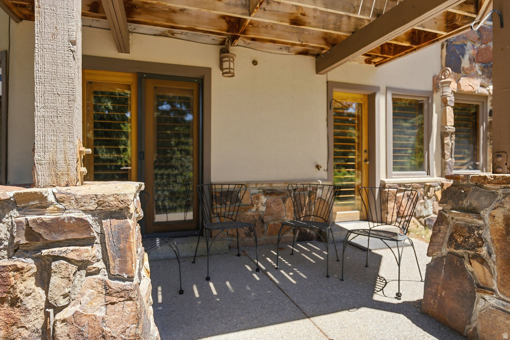 Expansive outdoor patio featuring a concrete slab, rustic stone accents, exposed wood beam ceiling, and multiple glass-paned doors