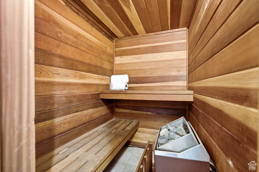 Dedicated sauna room featuring natural wood paneling, built-in benches, and a floor-mounted sauna heater with rocks