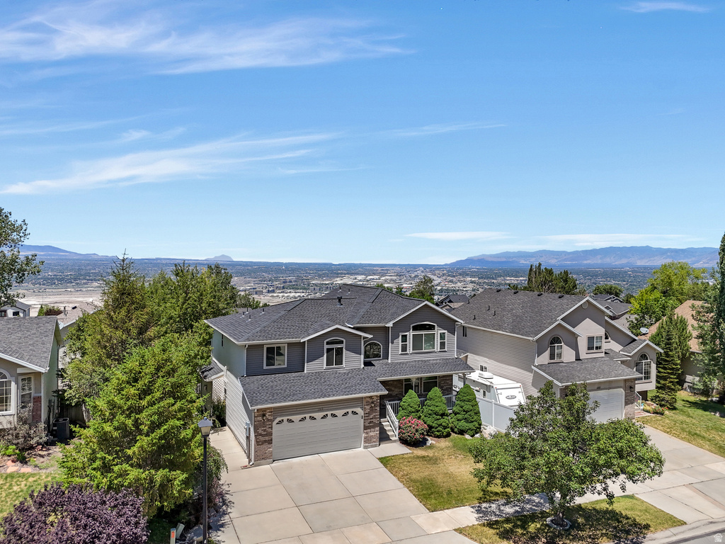 Two-story residence featuring a gray exterior with stone accents, a dual garage, and established landscaping