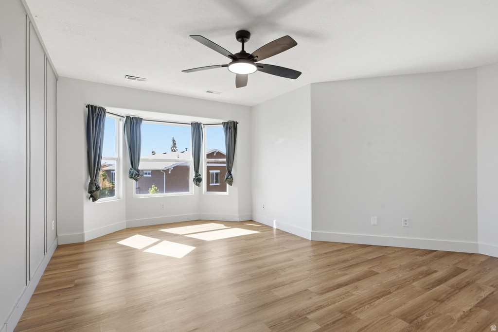 Spacious room featuring a prominent bay window, wood-finish flooring, and a ceiling fan with integrated lighting