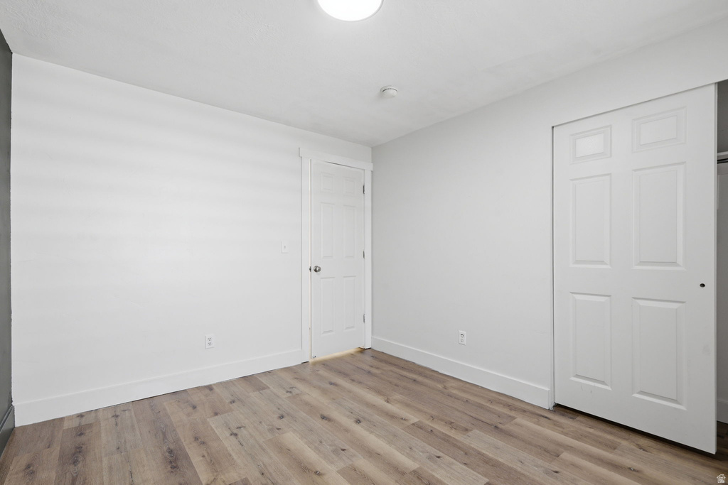 Interior room featuring wood-finish flooring, white baseboards, a white paneled door, and a white paneled sliding closet door