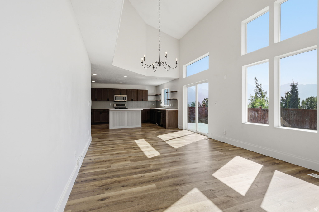 Open-concept living area featuring vaulted ceilings, wood-finish flooring, a contemporary chandelier, multiple large windows, and a sliding glass door