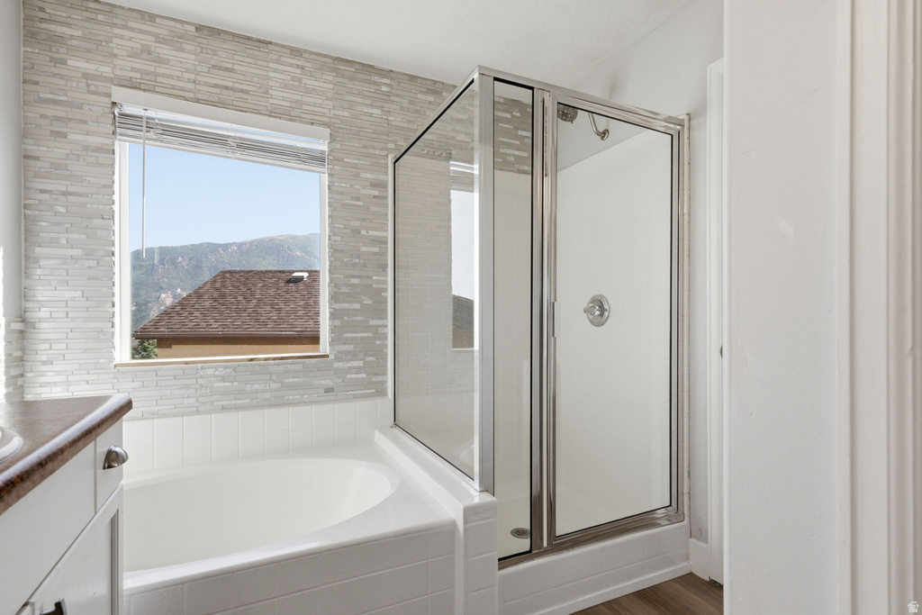 Bathroom featuring a built-in tub, a glass-enclosed shower with chrome fixtures, and wood-finish flooring