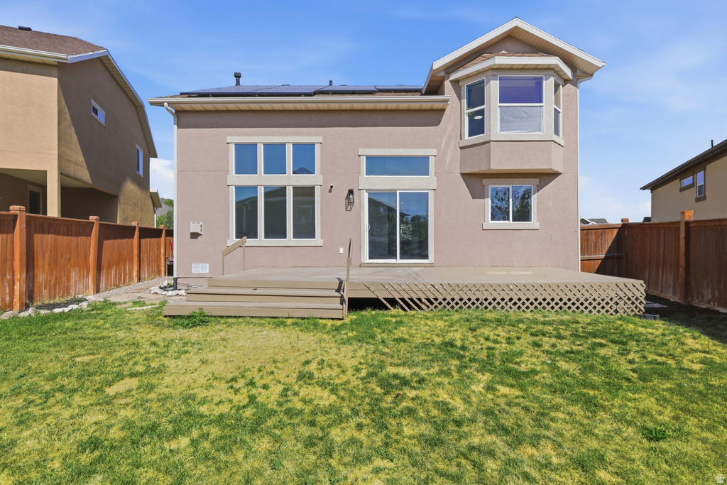 Rear exterior featuring a large wooden deck with lattice skirting, multiple windows, and a sliding glass door