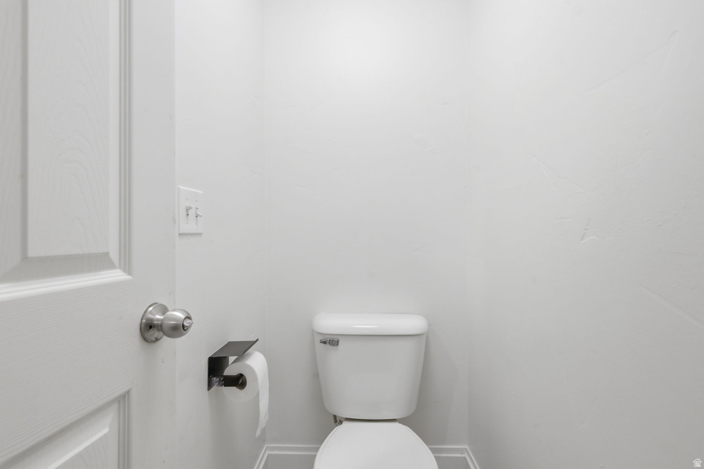 White paneled door with a brushed nickel doorknob, leading into a space with light gray baseboards and a classic white toilet