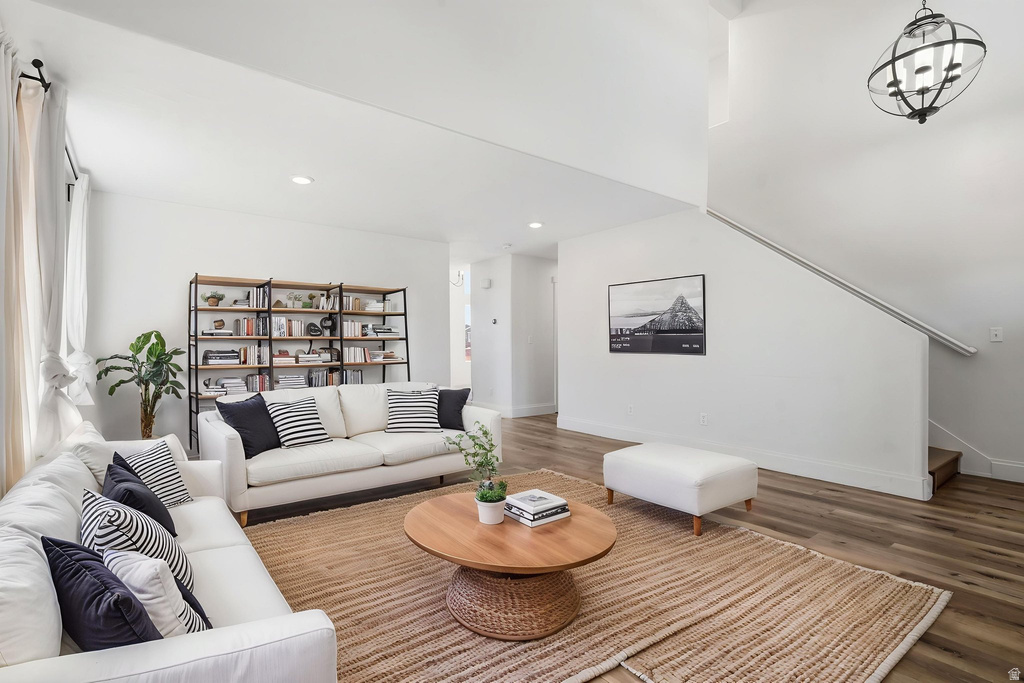 Open-concept living space featuring high ceilings, wood-finish flooring, a contemporary black metal and wood shelving unit, a modern orb chandelier, and a staircase with a sleek handrail