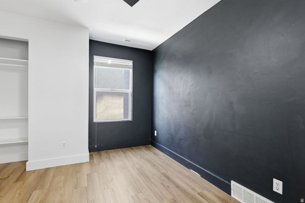 Room featuring wood-finish flooring, a contemporary dark accent wall, white baseboards, and a window with blinds