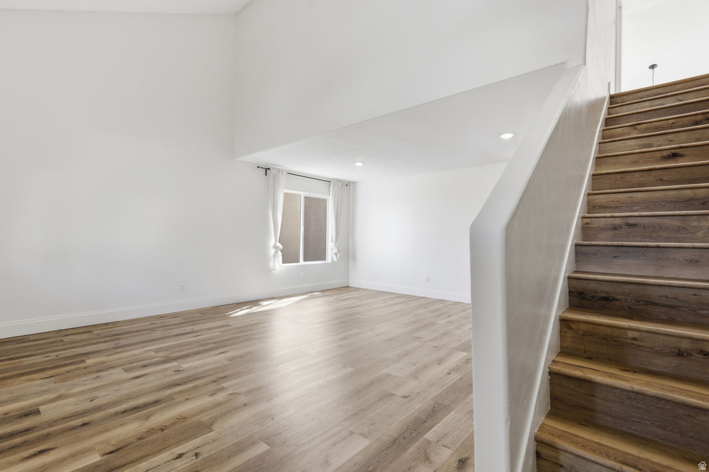Spacious living area featuring high ceilings, wood-finish flooring, recessed lighting, and a prominent staircase with matching wood-finish treads