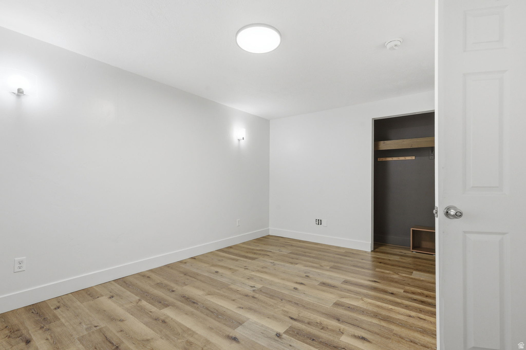 Room featuring wood-finish flooring, white baseboards, and a built-in closet with a clothes rod