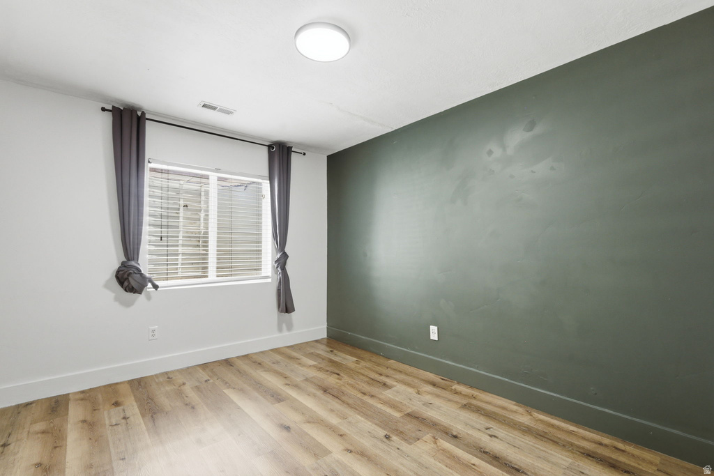 Spacious room featuring wood-finish flooring, a contemporary ceiling light fixture, and a window with blinds