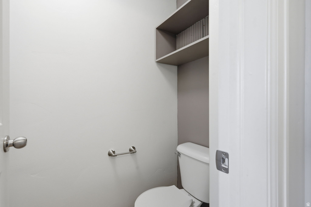 Powder room featuring a white toilet, wall-mounted shelving, and a brushed nickel towel bar