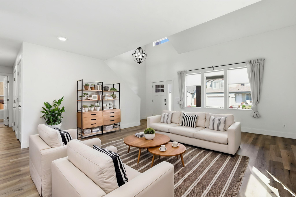 Vaulted ceiling living room featuring wood-finish flooring, a contemporary black orb chandelier, and an architectural skylight
