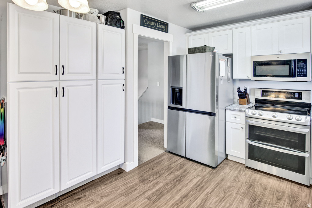 Kitchen featuring white cabinetry, stainless steel appliances, wood-finish flooring, and a light-toned countertop