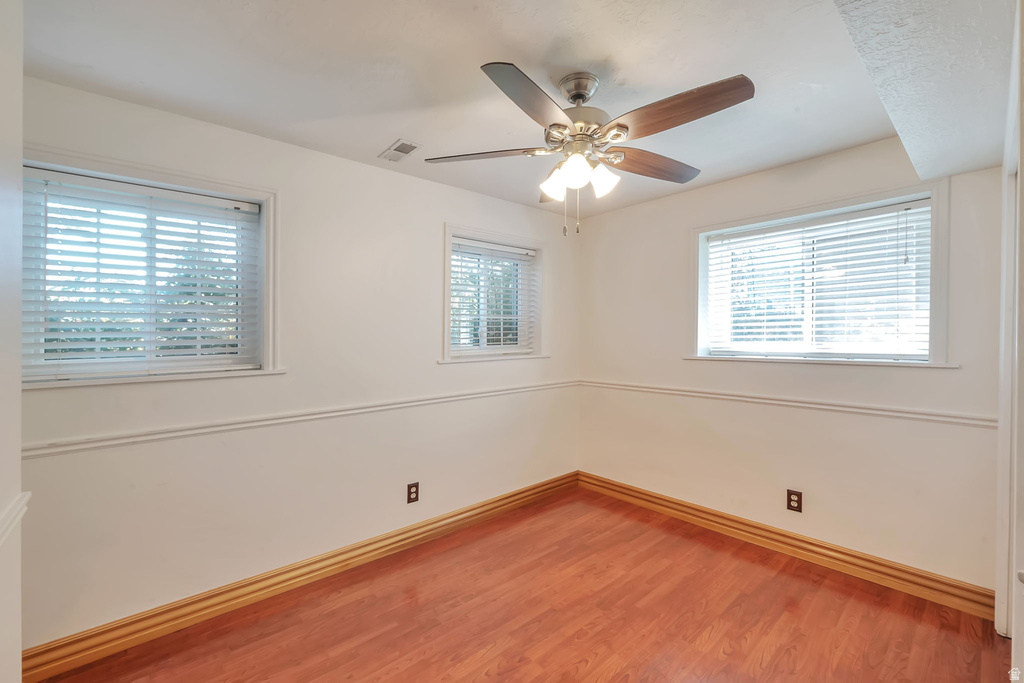 Room featuring wood-finish flooring, white walls with chair rail molding, and three windows with blinds