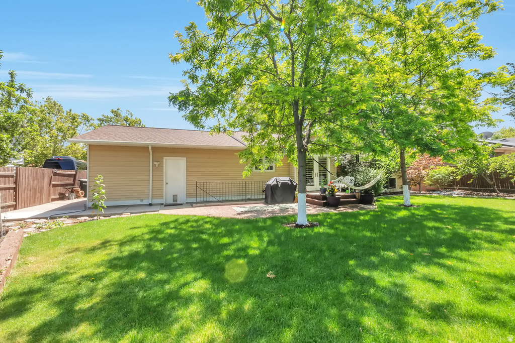 Expansive backyard featuring a large green lawn, mature trees, a multi-level deck, and a paved patio area