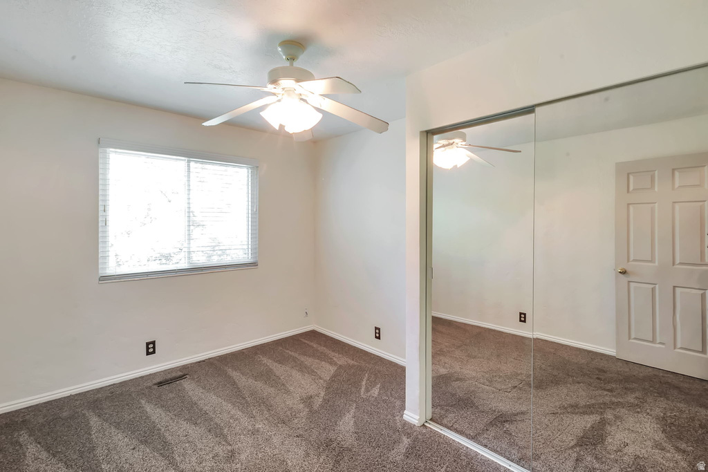 Carpeted room featuring a ceiling fan with integrated lighting, a window with horizontal blinds, and a mirrored sliding closet door