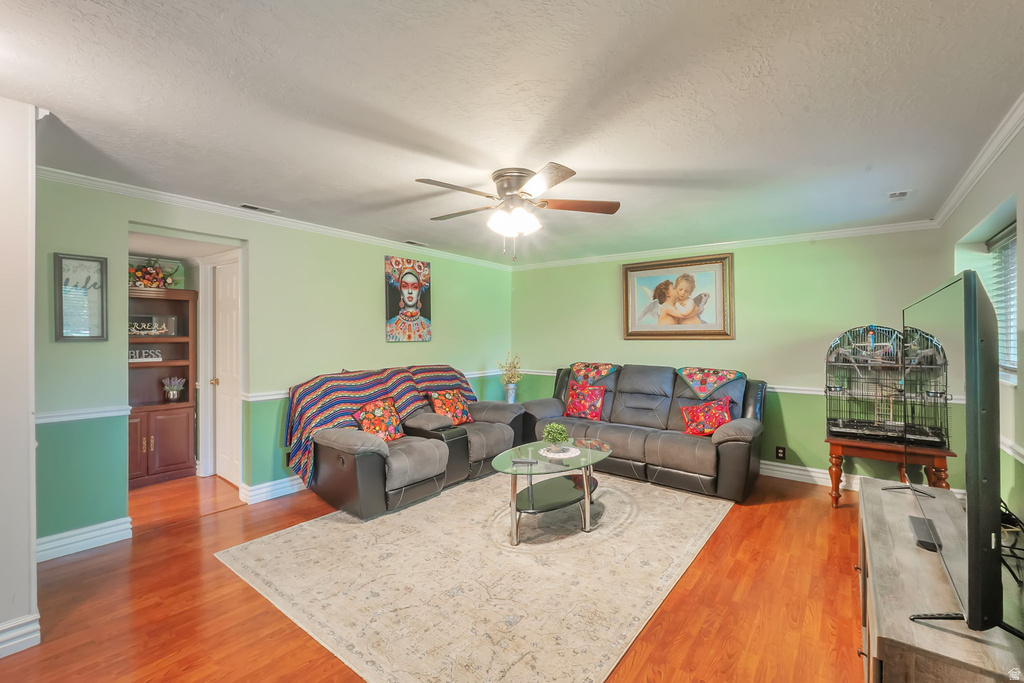 Open concept living area featuring wood-finish flooring, a ceiling fan with light fixture, and crown molding