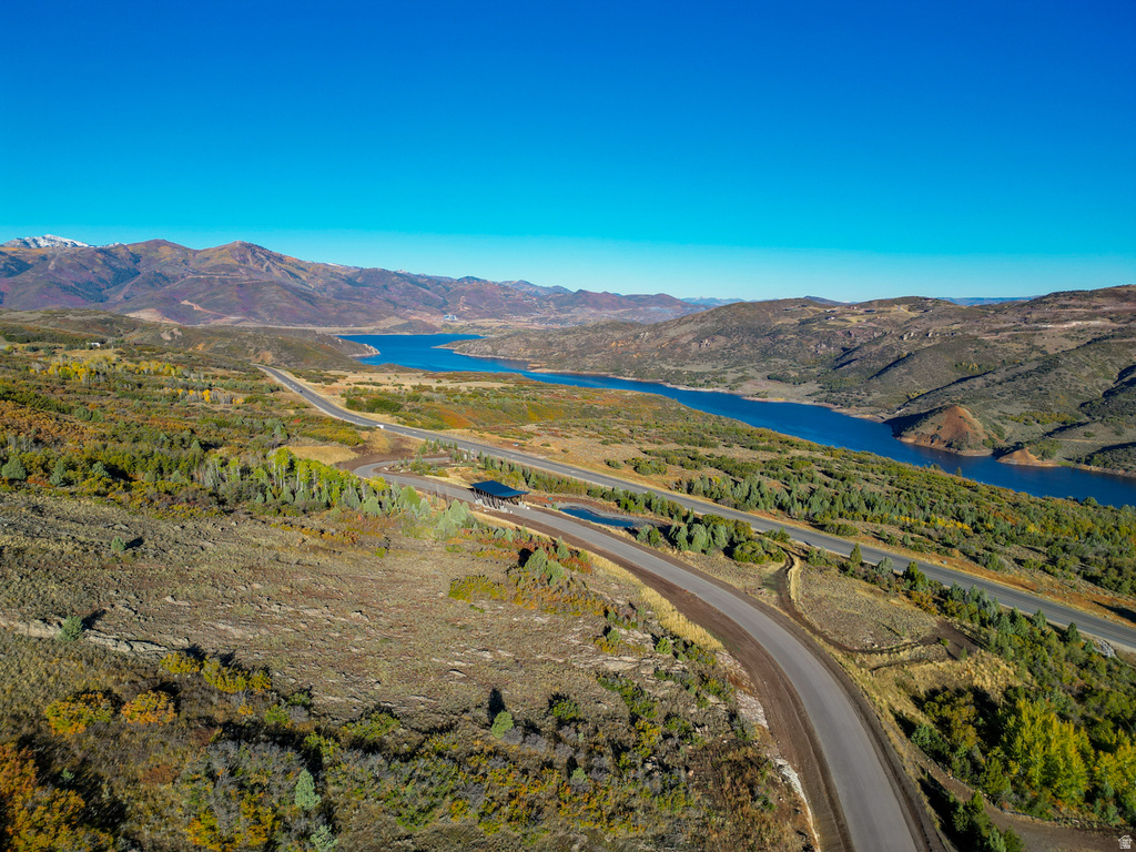 Expansive landscape featuring a winding paved road, distant lake, and surrounding mountainous terrain under a clear blue sky