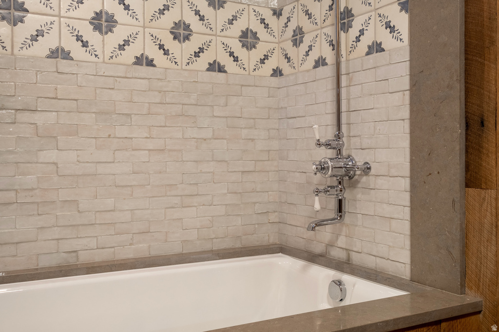 Bathtub with a chrome fixture, surrounded by subway-style tile and decorative patterned tilework