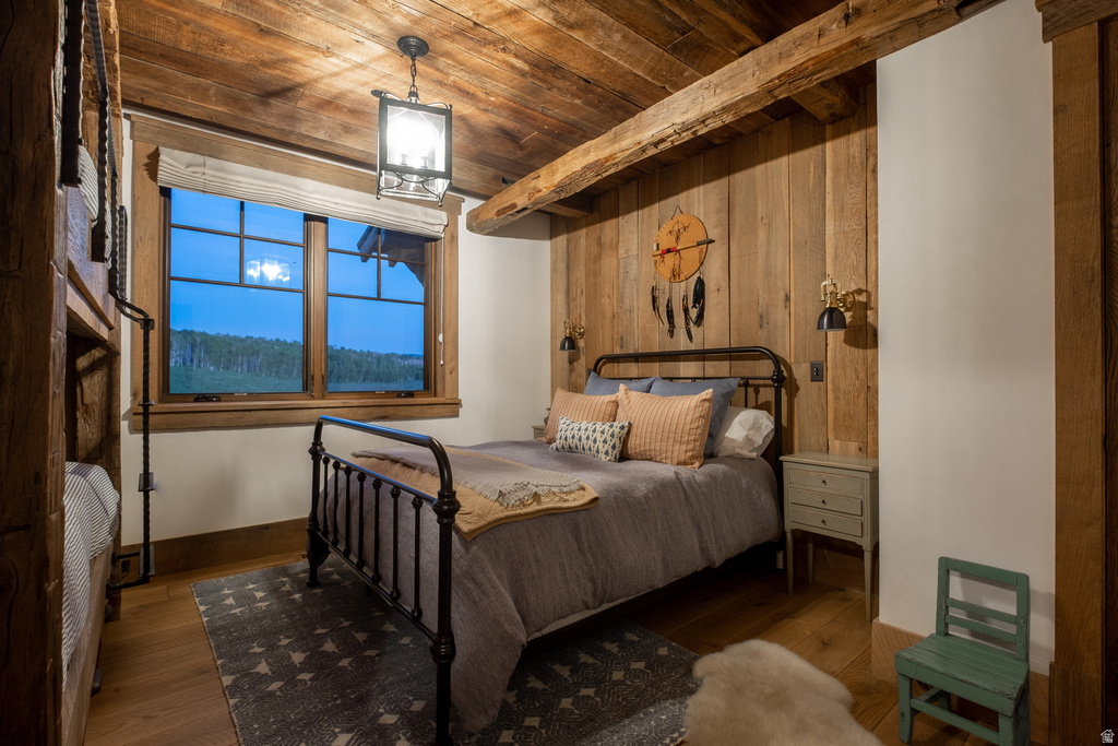 Bedroom featuring wood-finish flooring, wood-paneled walls, exposed wood beam ceiling, and a large multi-pane window