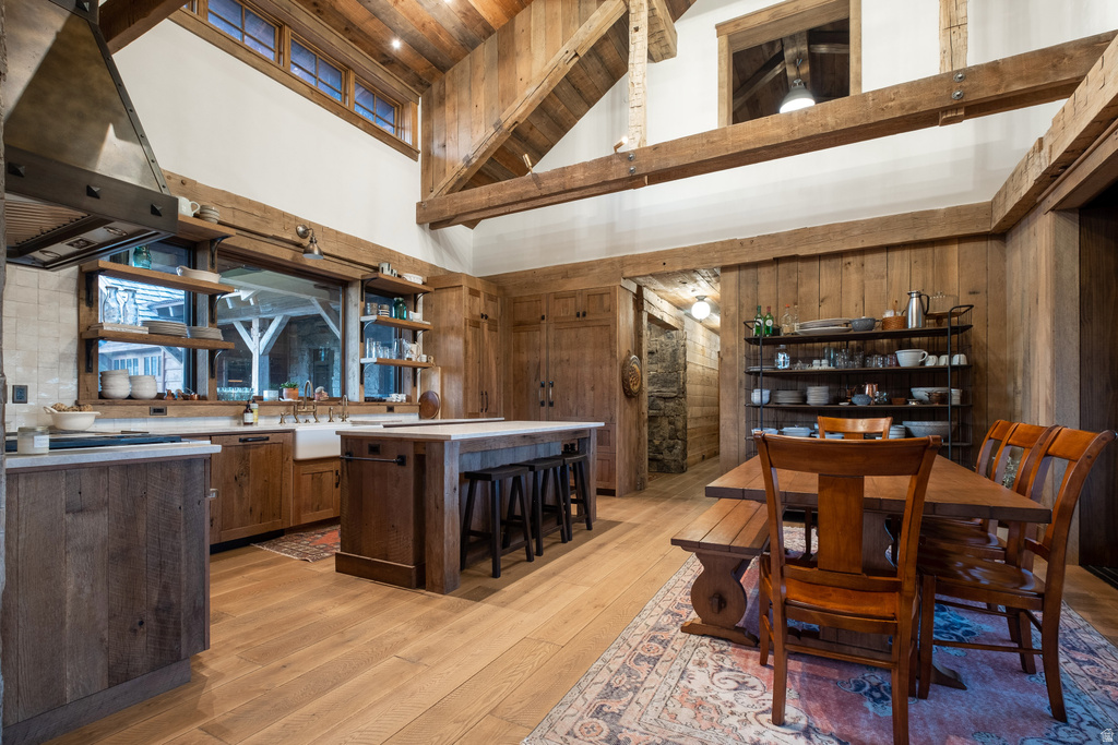 Open-concept kitchen with high ceilings, exposed wood beams, light wood-finish flooring, a farmhouse sink, and a center island with seating