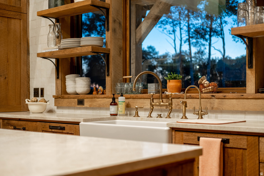 Kitchen featuring a white farmhouse sink with brass fixtures, wood-finish cabinetry, light-toned countertops, and open shelving