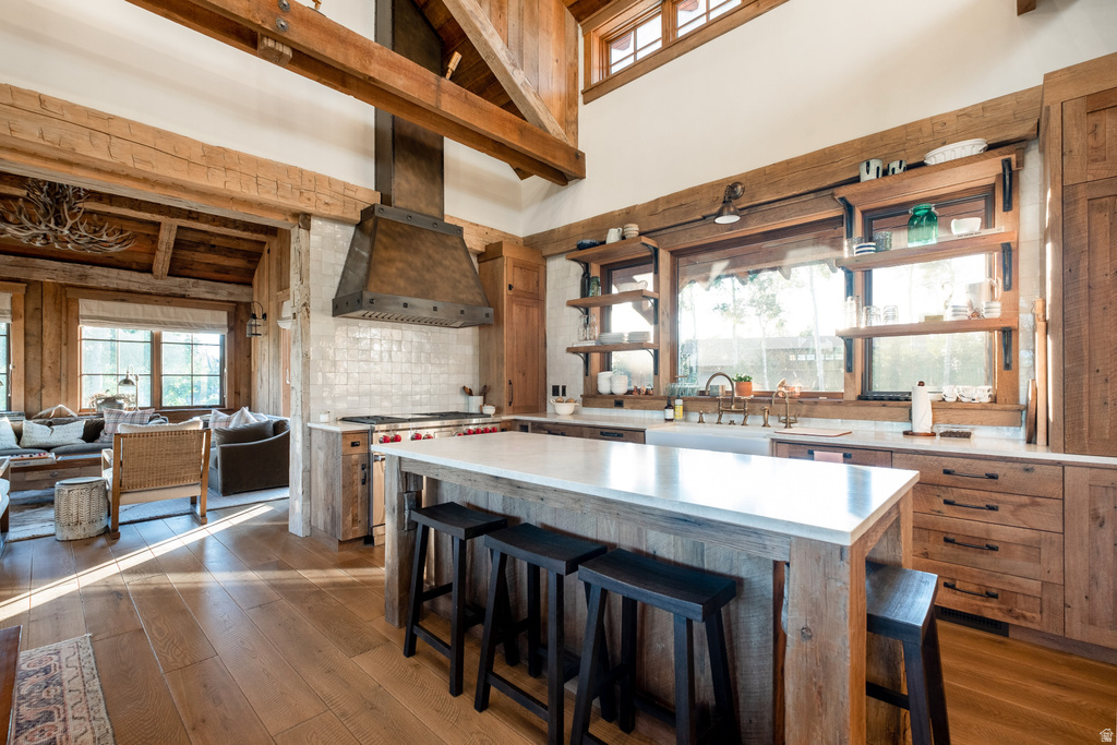 Gourmet kitchen featuring a large central island with a solid surface countertop, custom wood cabinetry, wood-finish flooring, a commercial-style range with a custom wood hood, and a white subway tile backsplash