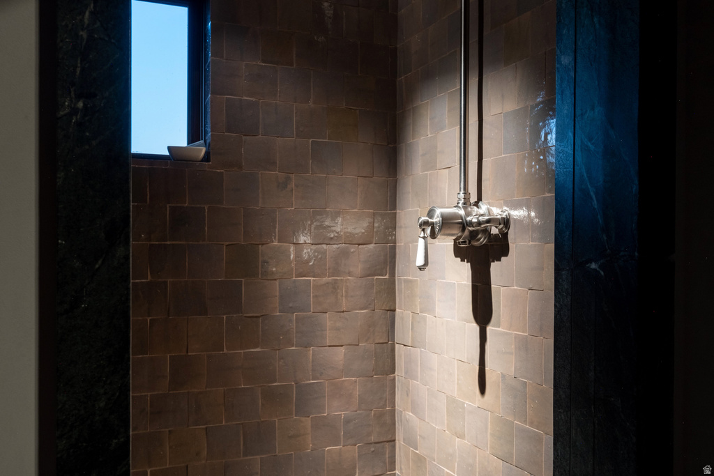 Shower enclosure featuring square-tiled walls, a polished chrome shower fixture with a white lever handle, and a dark-framed window