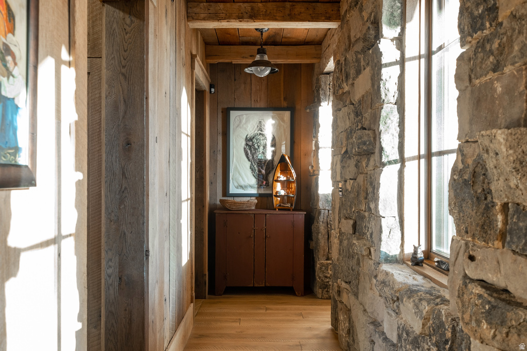 Hallway featuring stone walls, wood-finish flooring, wood-paneled walls, and a wood-beamed ceiling