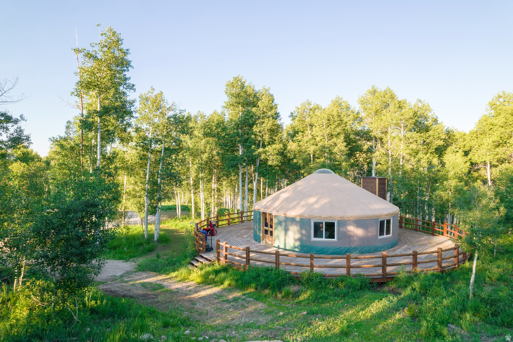 Yurt structure surrounded by dense foliage, featuring a circular wooden deck with a rustic log railing