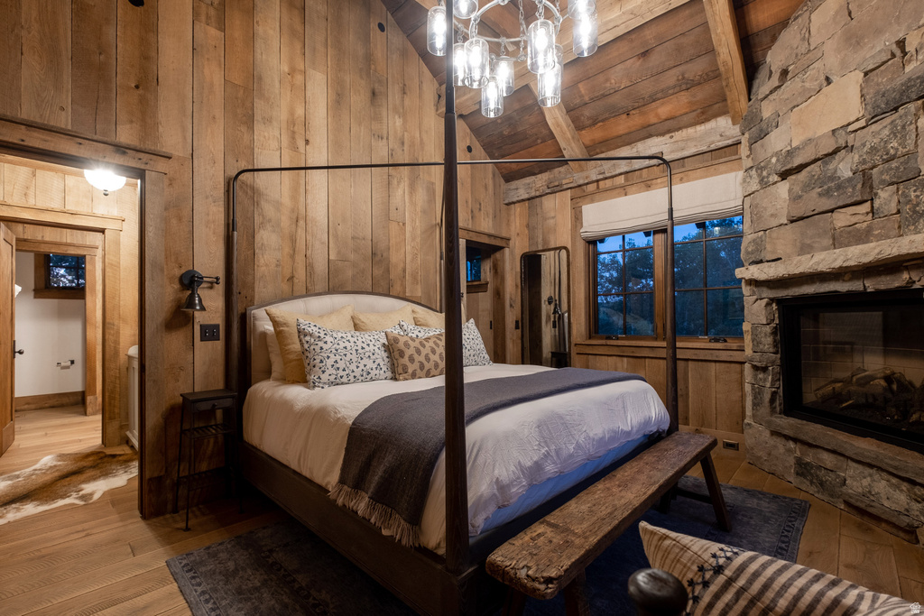 Vaulted wood-paneled ceilings with exposed beams, a stone fireplace, wood-finish flooring, and a large window
