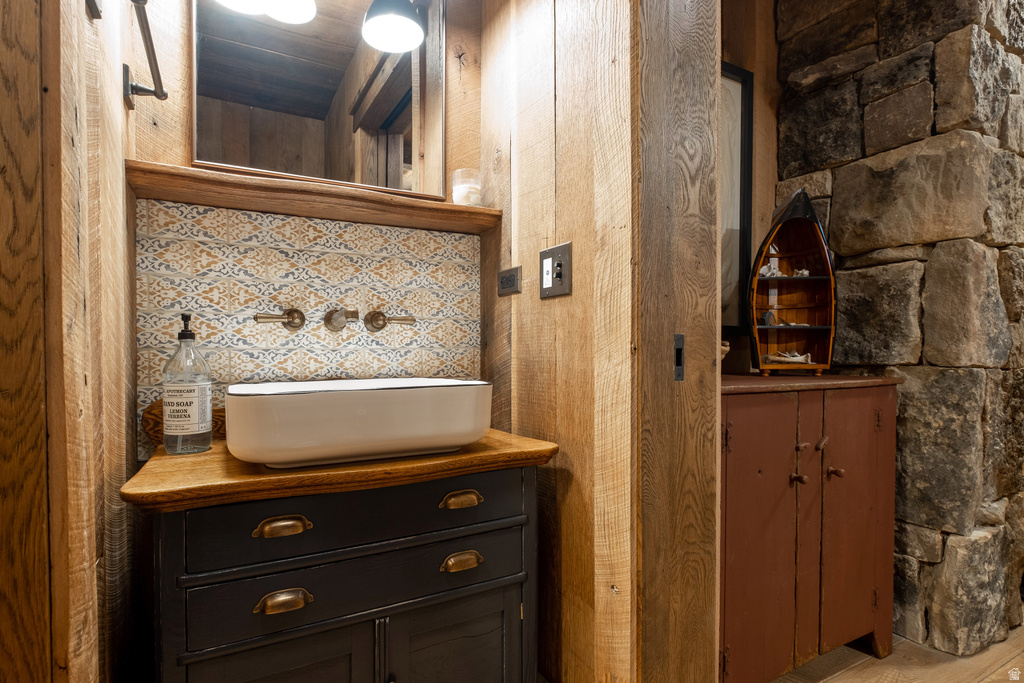 Rustic-inspired bathroom featuring wood-panel walls, a stone accent wall, and a vessel sink with wall-mounted brass fixtures
