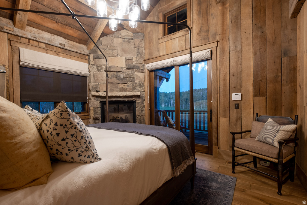 Bedroom featuring wood-finish flooring, plank wood walls, and a stone fireplace