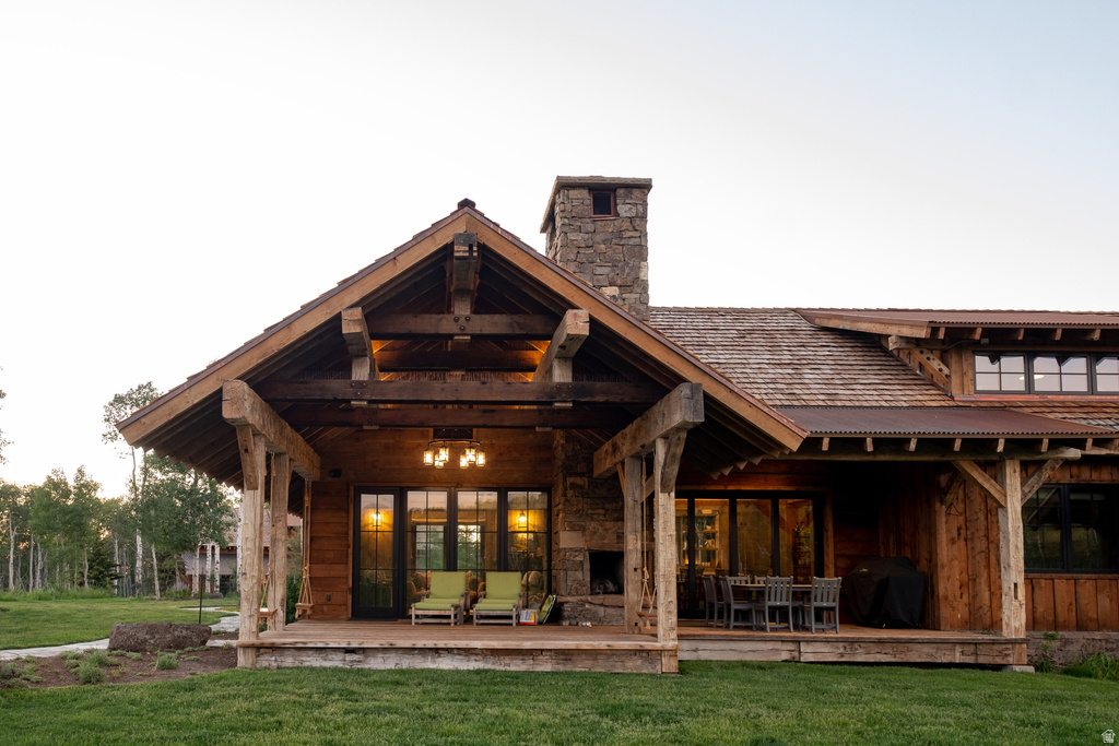 Expansive covered patio featuring a stone fireplace, exposed timber beams, wood-finish siding, a shake shingle roof, and multiple large windows
