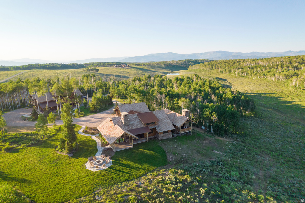 Expansive property featuring a rustic-style residence, mature trees, a stone fire pit, extensive green space, and a distant mountain range