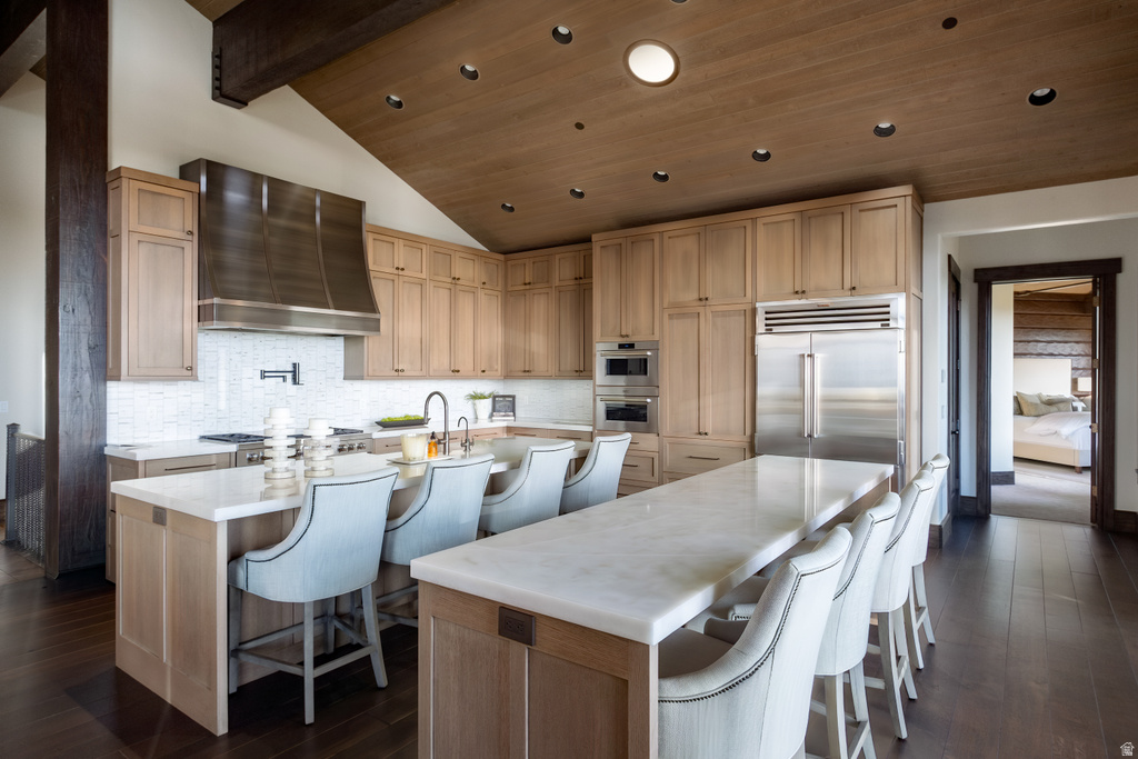 Gourmet kitchen featuring a large central island with seating, stainless steel appliances, extensive cabinetry, light wood-finish flooring, and a vaulted wood-paneled ceiling